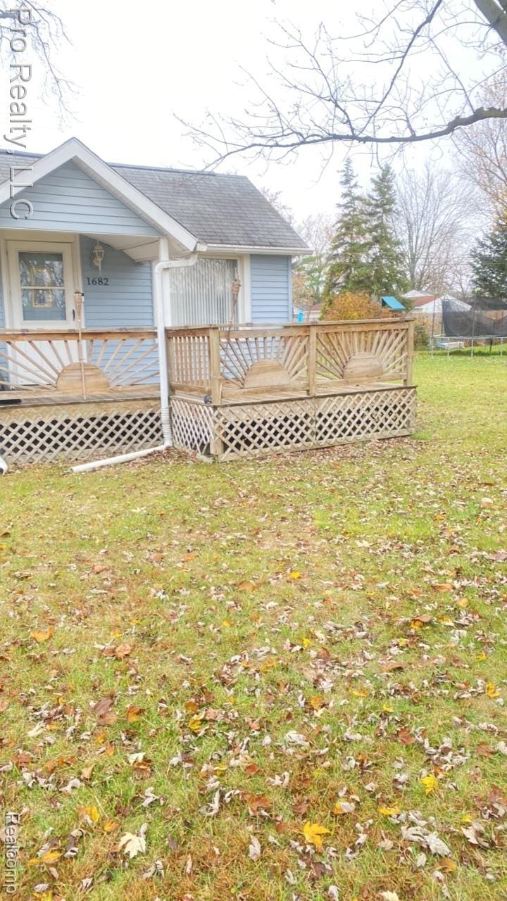 1682 Beatrice St, Westland, MI 48186 - rear view of property featuring a wooden deck, a trampoline, a lawn, and roof with shingles