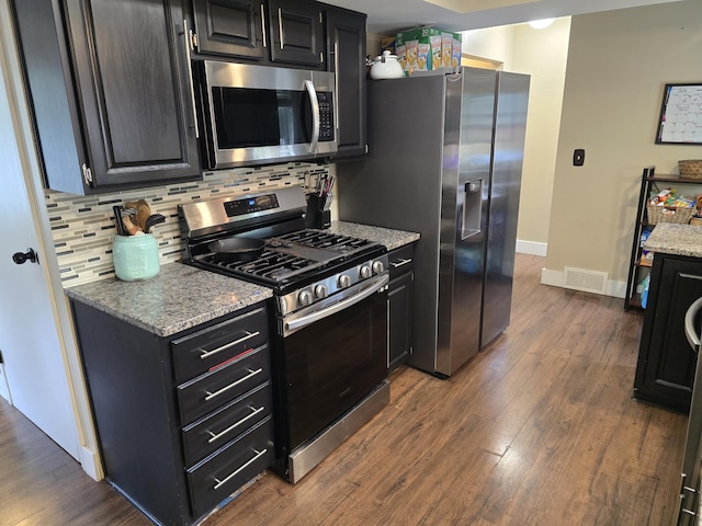 3330 Bradford St NE, Grand Rapids, MI 49525 - kitchen featuring appliances with stainless steel finishes, dark cabinetry, dark wood-style flooring, decorative backsplash, and light stone counters
