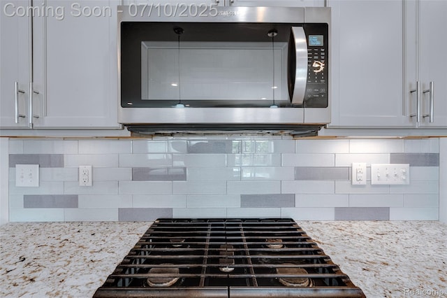 43433 Chancellor Ln, Novi, MI 48375 - kitchen view of stainless steel microwave, decorative backsplash, stovetop, light stone counters, and white cabinets