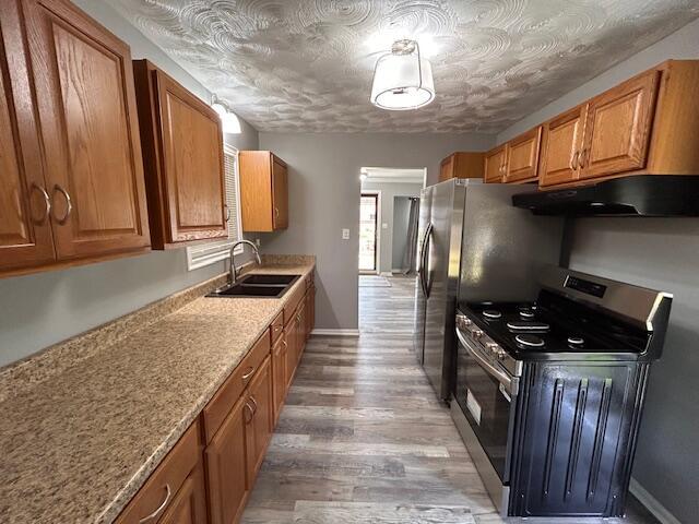 26219 Clarita St, Redford, MI 48240 - kitchen with stainless steel range with electric cooktop, under cabinet range hood, brown cabinetry, light wood-style floors, and a textured ceiling