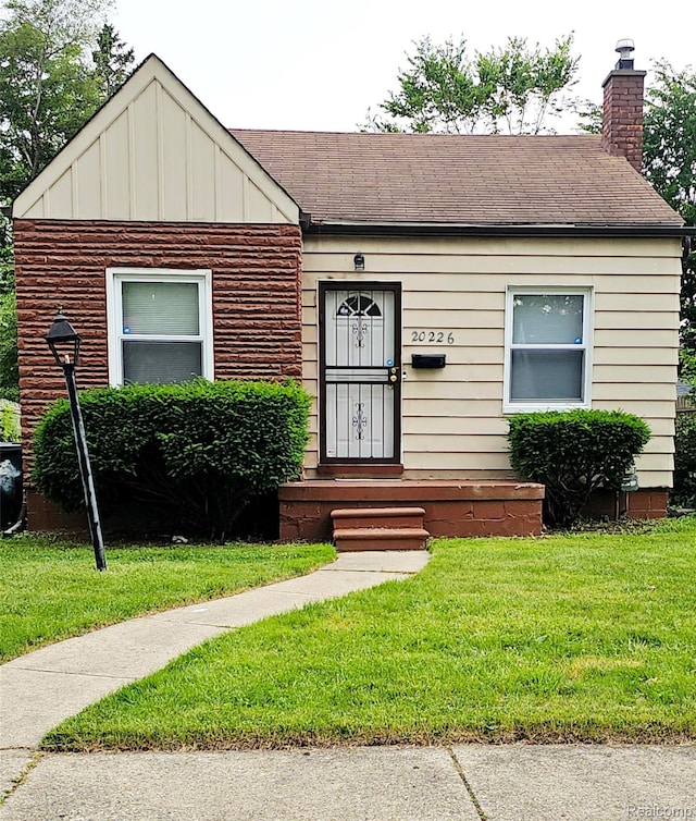 20226 Mccormick, Detroit, MI 48224 - view of front facade with a front lawn, roof with shingles, a chimney, and board and batten siding