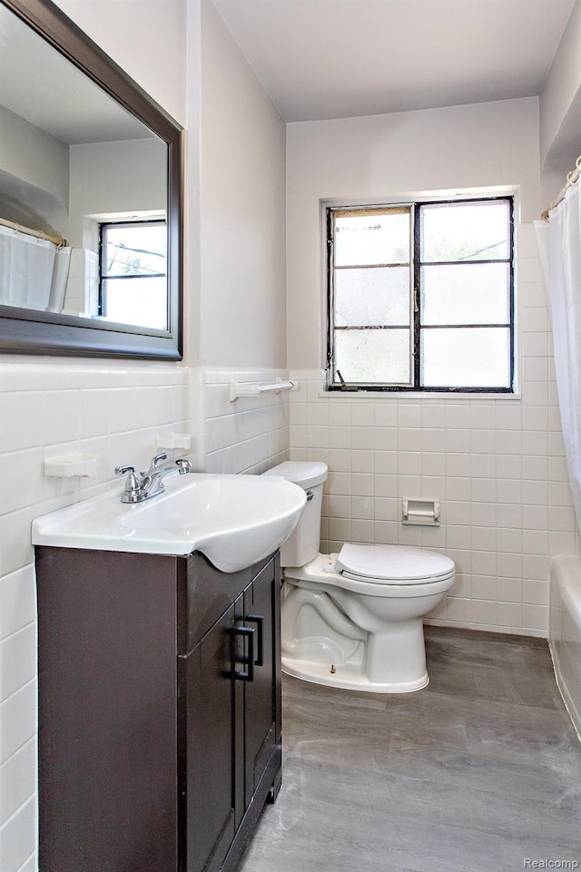 23461 Avon Rd, Oak Park, MI 48237 - bathroom featuring tile walls, vanity, wood finished floors, shower / bath combo with shower curtain, and wainscoting