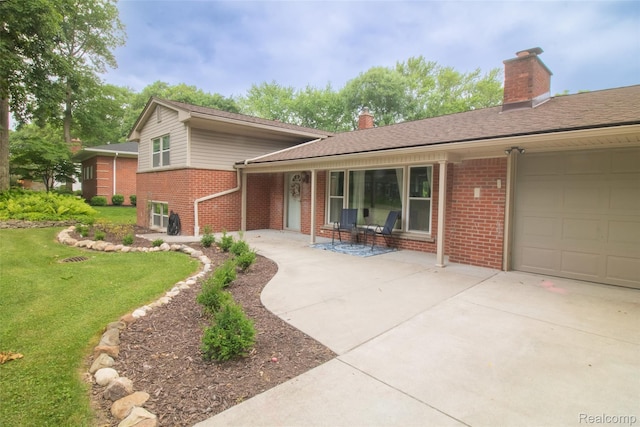 21102 Knudsen Dr, Grosse Ile, MI 48138 - split level home featuring brick siding, a chimney, a front lawn, driveway, and covered porch