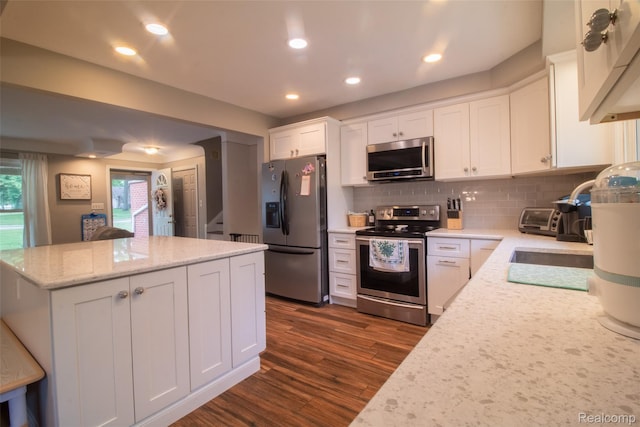 21102 Knudsen Dr, Grosse Ile, MI 48138 - kitchen featuring appliances with stainless steel finishes, dark wood finished floors, backsplash, white cabinetry, and a kitchen island
