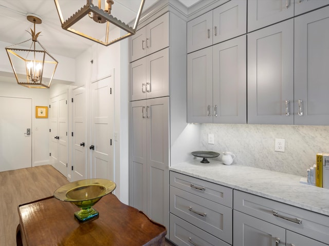 111 N Ashley St Unit 513, Ann Arbor, MI 48104 - kitchen featuring gray cabinets, decorative backsplash, a chandelier, light wood-type flooring, and light stone countertops