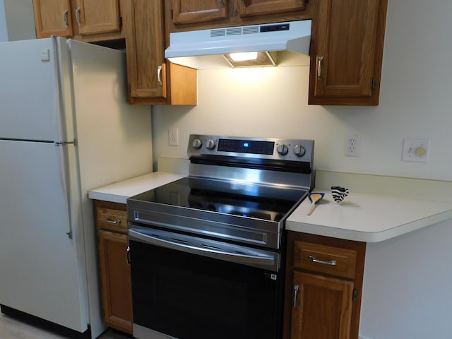 36561 S Deerhurst S, Westland, MI 48185 - kitchen with stainless steel electric stove, under cabinet range hood, freestanding refrigerator, light countertops, and brown cabinetry