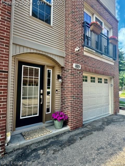 105 S 2nd St, Brighton, MI 48116 - doorway to property with an attached garage, brick siding, a balcony, and asphalt driveway
