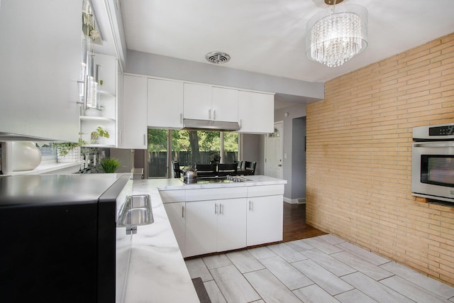 3715 Lancaster Dr, Kalamazoo, MI 49006 - kitchen featuring brick wall, oven, under cabinet range hood, white cabinets, and open shelves