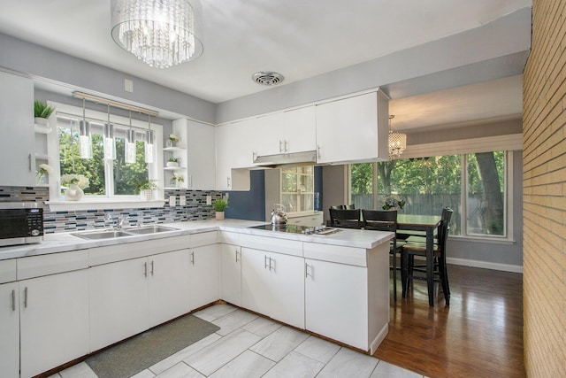 3715 Lancaster Dr, Kalamazoo, MI 49006 - kitchen with a chandelier, open shelves, stainless steel microwave, black electric stovetop, and backsplash