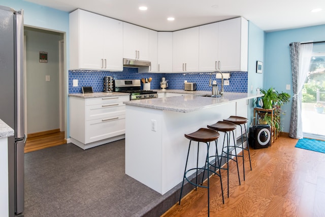 39079 Ross St, Livonia, MI 48154 - kitchen with stainless steel appliances, a peninsula, a kitchen breakfast bar, decorative backsplash, and white cabinetry