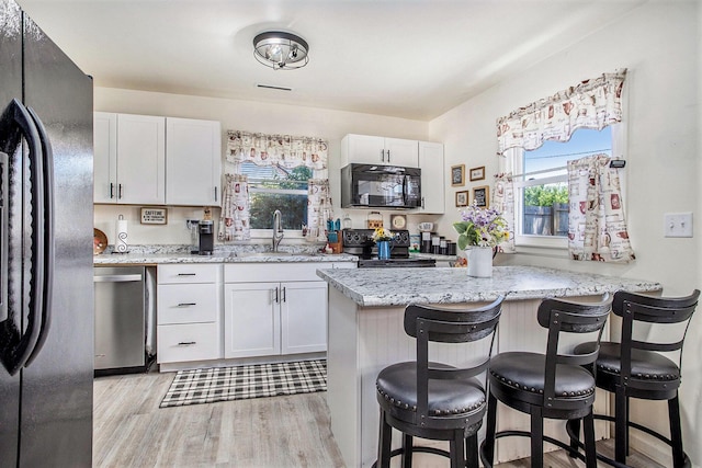 320 E Dr, Marshall, MI 49068 - kitchen featuring black appliances, light wood-style flooring, a kitchen breakfast bar, light stone counters, and white cabinetry