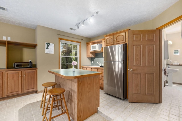 6177 Heathcross Dr, Hudsonville, MI 49426 - kitchen with freestanding refrigerator, white microwave, a kitchen island, a breakfast bar, and a textured ceiling