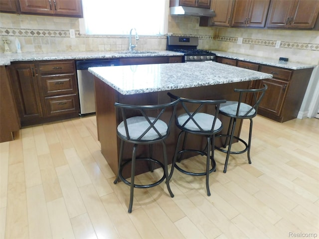2238 Nadine Dr, Sterling Heights, MI 48310 - kitchen featuring appliances with stainless steel finishes, under cabinet range hood, a center island, decorative backsplash, and a kitchen breakfast bar