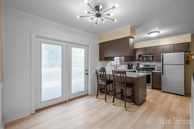 2958 Bluewater Ln SW, Grandville, MI 49418 - kitchen with stainless steel appliances, a peninsula, light wood finished floors, a breakfast bar, and a chandelier