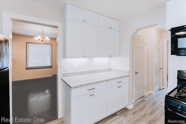 16219 Normandy St, Detroit, MI 48221 - kitchen with black gas range oven, white cabinets, light wood finished floors, arched walkways, and a chandelier