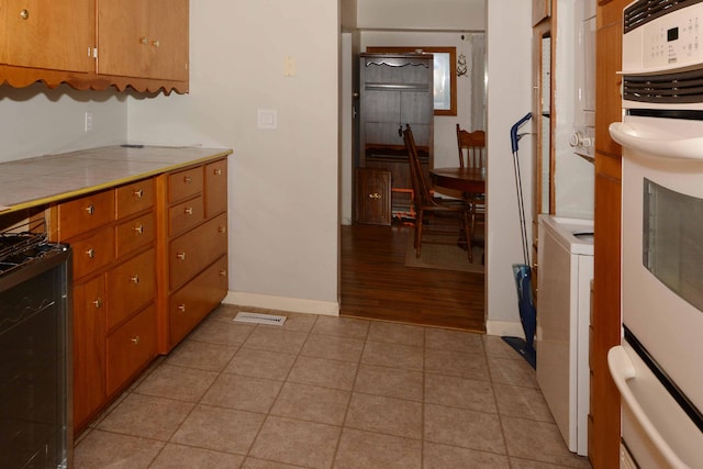 2357 River St, Kalamazoo, MI 49048 - kitchen with tile countertops, brown cabinetry, light tile patterned floors, and gas stove