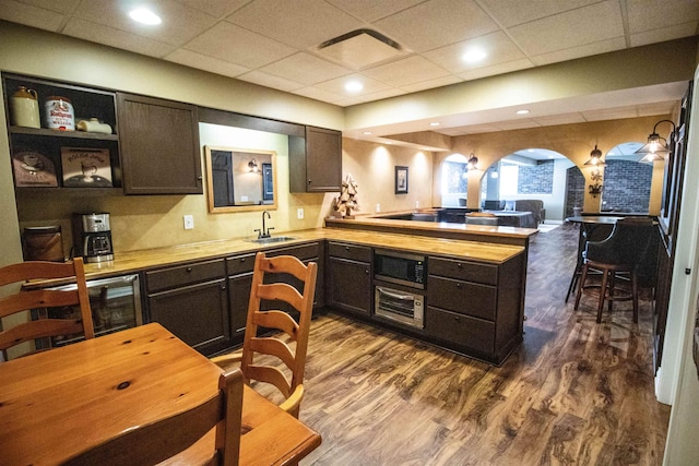 7380 Vassar Rd, Grand Blanc, MI 48439 - kitchen featuring a peninsula, arched walkways, dark wood-style flooring, dark brown cabinetry, and a drop ceiling