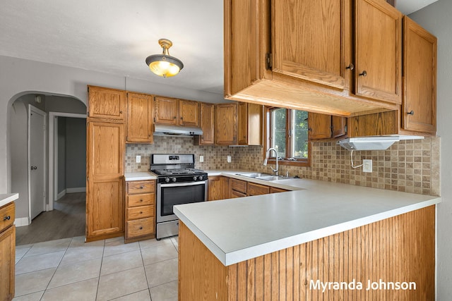 602 Elsa St, North Muskegon, MI 49445 - kitchen featuring stainless steel gas range oven, under cabinet range hood, light countertops, decorative backsplash, and brown cabinets