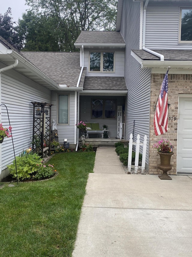 9379 Jamie Dr, Davison, MI 48423 - view of exterior entry with a shingled roof, a porch, a lawn, and a garage