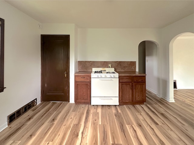 2839 128th Ave, Holland, MI 49424 - kitchen with white gas range, brown cabinetry, arched walkways, and light wood-type flooring