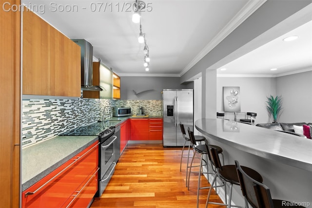 532 E Fox Hills Dr, Bloomfield Hills, MI 48304 - kitchen featuring appliances with stainless steel finishes, wall chimney exhaust hood, light wood-style floors, a kitchen breakfast bar, and decorative backsplash
