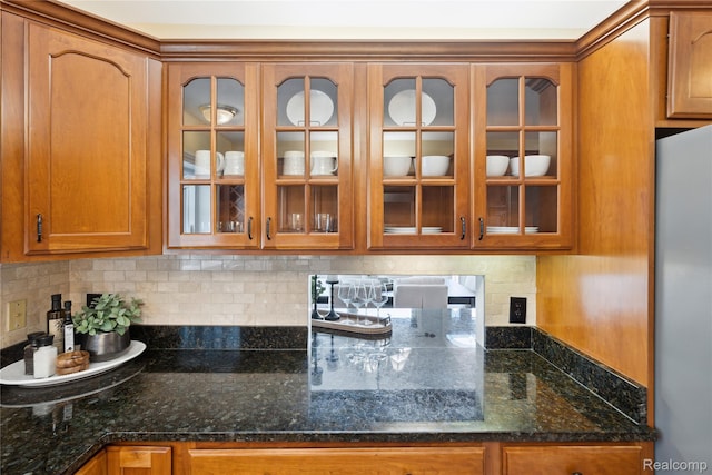2009 Ridge Rd, White Lake, MI 48383 - kitchen with freestanding refrigerator, glass insert cabinets, brown cabinetry, decorative backsplash, and dark stone counters
