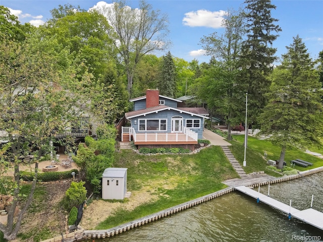 2009 Ridge Rd, White Lake, MI 48383 - back of property featuring a chimney, a deck with water view, a shed, a lawn, and an outdoor fire pit