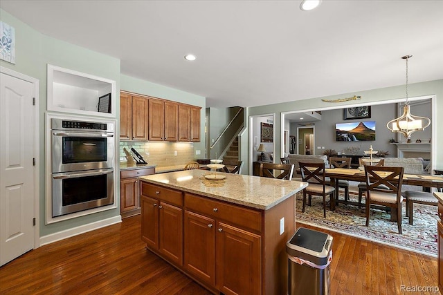 8507 Newbury Ct N, Canton, MI 48187 - kitchen with stainless steel double oven, decorative backsplash, dark wood-style floors, light stone countertops, and a center island