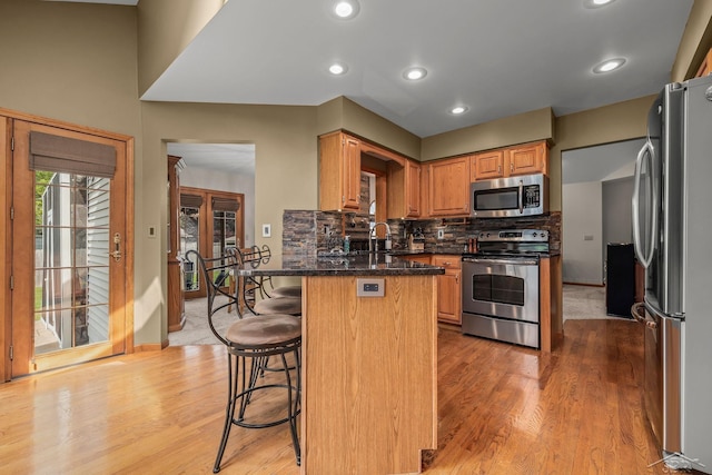 1381 Briarson Dr, Saginaw, MI 48638 - kitchen with appliances with stainless steel finishes, light wood-style floors, a kitchen breakfast bar, decorative backsplash, and dark stone countertops
