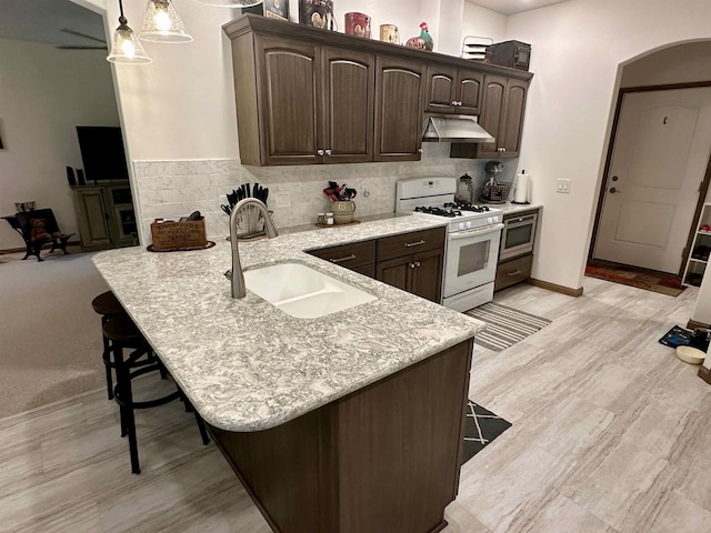 308 W Hosmer St, Saint Charles, MI 48655 - kitchen with white gas stove, range hood, arched walkways, a kitchen bar, and dark brown cabinetry