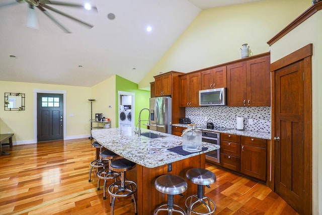 9434 84th St SE, Alto, MI 49302 - kitchen featuring washer / clothes dryer, stainless steel appliances, a kitchen bar, light wood-style floors, and a center island with sink
