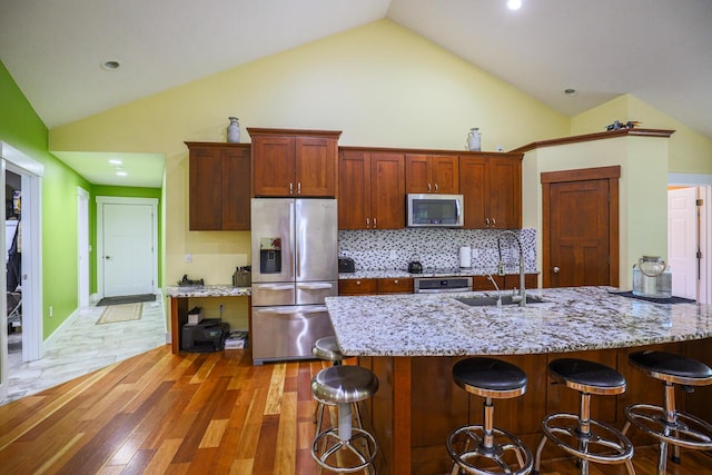 9434 84th St SE, Alto, MI 49302 - kitchen with appliances with stainless steel finishes, a kitchen bar, light stone counters, high vaulted ceiling, and light wood-style floors