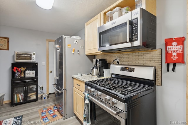204 W Caroline St, Bellevue, MI 49021 - kitchen featuring appliances with stainless steel finishes, light brown cabinets, light wood-style floors, backsplash, and light stone countertops