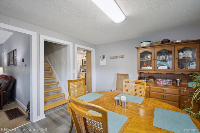 204 W Caroline St, Bellevue, MI 49021 - dining space with wood finished floors, stairway, and a textured ceiling