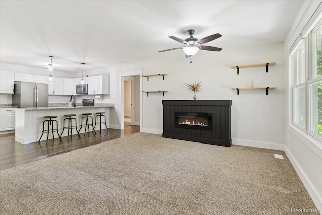 3416 Abbottsford Rd, Clyde, MI 48049 - living room featuring dark colored carpet, a ceiling fan, and a glass covered fireplace