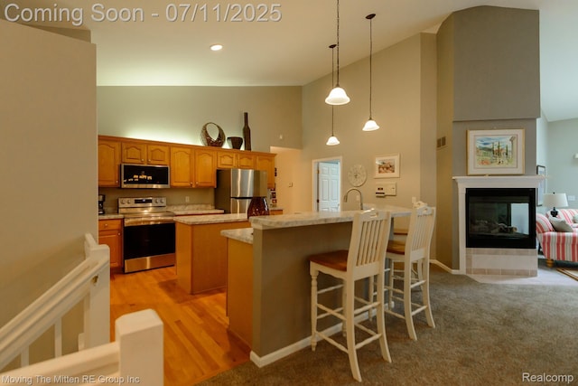 61001 Evergreen Ct, South Lyon, MI 48178 - kitchen featuring appliances with stainless steel finishes, high vaulted ceiling, a kitchen island with sink, hanging light fixtures, and a multi sided fireplace