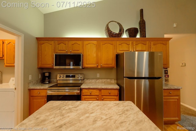 61001 Evergreen Ct, South Lyon, MI 48178 - kitchen with appliances with stainless steel finishes, light countertops, vaulted ceiling, independent washer and dryer, and brown cabinetry