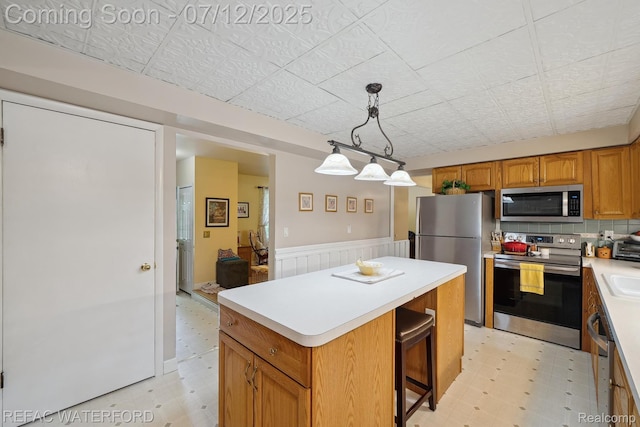 11857 Ely Rd, Davisburg, MI 48350 - kitchen with appliances with stainless steel finishes, light floors, a wainscoted wall, a center island, and light countertops