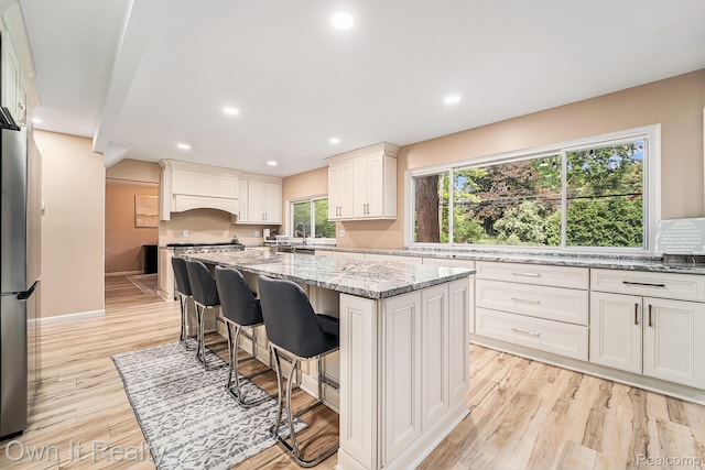 14128 Ellen Dr, Dearborn Heights, MI 48154 - kitchen featuring a kitchen island, light stone countertops, light wood-style flooring, freestanding refrigerator, and a kitchen bar