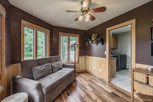 2086 Haines Rd, Lapeer, MI 48446 - living area with washer and clothes dryer, a wainscoted wall, light wood-style flooring, a ceiling fan, and wooden walls