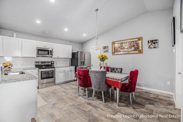 4061 Tributary Dr, Holland, MI 49424 - kitchen with appliances with stainless steel finishes, vaulted ceiling, light wood finished floors, white cabinetry, and decorative backsplash