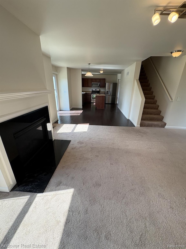 8213 Bayberry Ct, Dexter, MI 48130 - unfurnished living room featuring dark carpet, a fireplace with flush hearth, and stairs