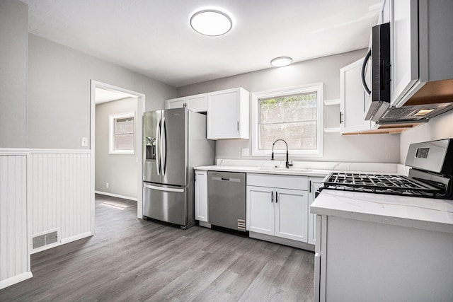 1505 Platt St, Niles, MI 49120 - kitchen featuring stainless steel appliances, light wood-type flooring, white cabinetry, light stone counters, and a wainscoted wall