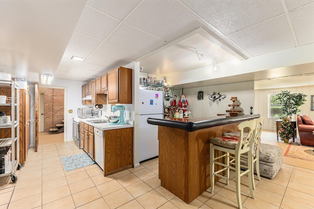 1818 Greenbriar Dr, Portage, MI 49024 - kitchen with white appliances, a breakfast bar area, brown cabinetry, light tile patterned floors, and a paneled ceiling