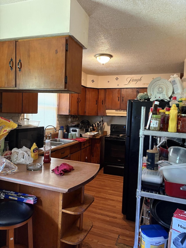 1596 Kay Dr, Benton Harbor, MI 49022 - kitchen featuring black appliances, under cabinet range hood, a textured ceiling, a peninsula, and light wood-style floors