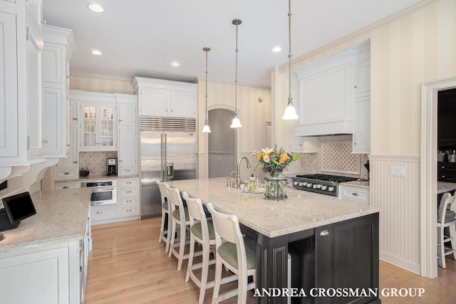 41 Bay Meadows Dr, Holland, MI 49424 - kitchen featuring appliances with stainless steel finishes, white cabinets, an island with sink, light wood-style flooring, and ornamental molding
