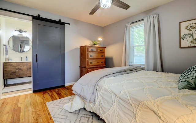 1441 Lewison Ave NE, Grand Rapids, MI 49505 - bedroom featuring a barn door, light wood-style floors, ensuite bathroom, and ceiling fan