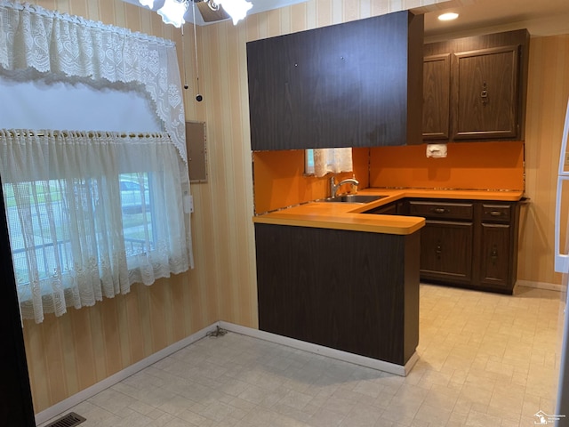 3897 15th St, Wyandotte, MI 48192 - kitchen featuring light floors, light countertops, wallpapered walls, dark brown cabinetry, and a peninsula
