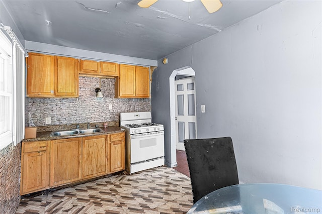 16934 Pembroke Ave, Detroit, MI 48235 - kitchen with white gas range, dark countertops, tasteful backsplash, ceiling fan, and arched walkways