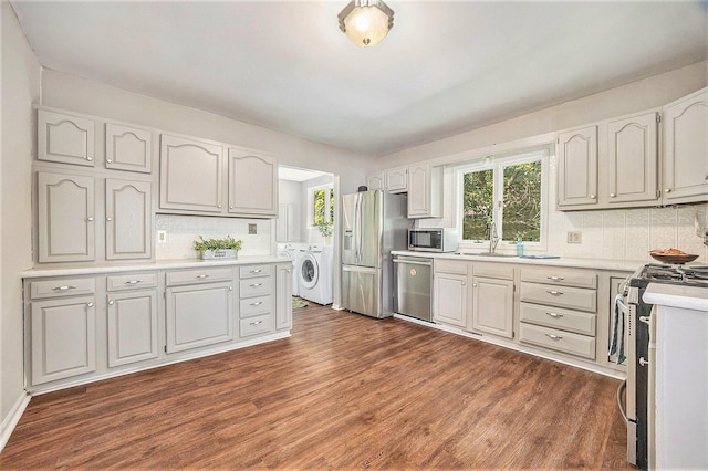 416 Kent St, Lowell, MI 49331 - kitchen featuring appliances with stainless steel finishes, washing machine and clothes dryer, backsplash, dark wood-type flooring, and light countertops